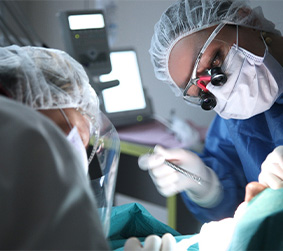 Dentist with mask and hairnet performing dental implant surgery